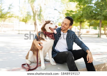 Latin adult man hugging and talking to his pretty husky dog while sitting in the park