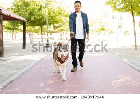 Full length of a happy furry dog with a leash walking with his male dog owner in the park running track