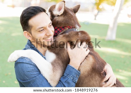 Side view of a good looking latin adult man hugging his dog buddy in the park