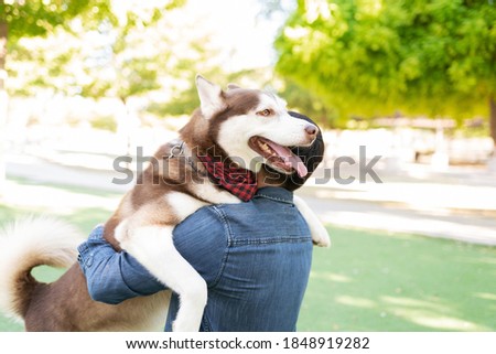 Rear view of a dog owner hugging his smiling furry dog in the park