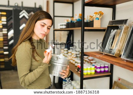 Good-looking young woman in her 20s is looking to buy paint and art supplies in the store to start painting a new canvas