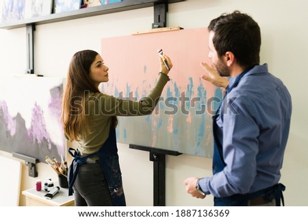 Young woman in her 20s is paying attention to a male teacher in class to learn how to do an art technique for her painting