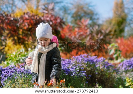 Little girl walks in the autumn colorful garden. He holds a soft toy in one hand touches the flowers with the other hand.