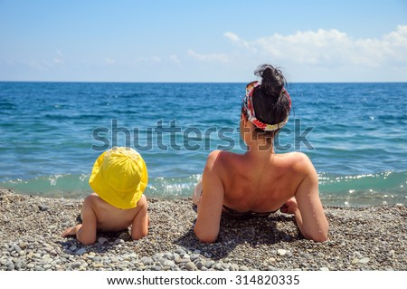 Mother and daughter sunbathe on the beach, they lie on his elbows and look at the sea