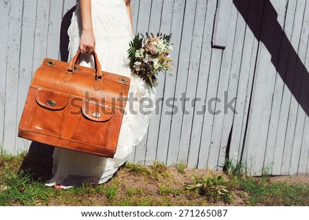 bouquet of flowers and vintage red suitcase in hands of the bride in a white dress