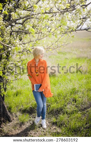 close-up portrait outdoors young beautiful girl in an orange hipster blonde bright cheerful polka dot blouse and with a laptop in the hands working smiling in sunglasses on a background trees