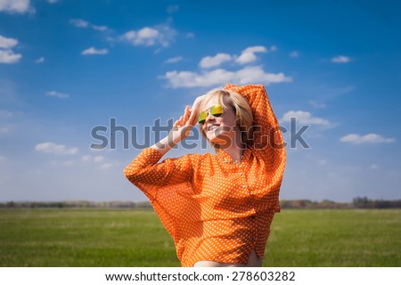 close-up portrait outdoors young beautiful girl in an orange hipster blonde bright cheerful polka dot blouse and smiling in SLR sunglasses against the blue sky  with white teeth