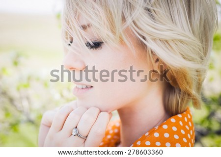 close-up portrait outdoors young beautiful girl in an orange hipster blonde bright cheerful polka dot blouse , smiling  plump lips on the background of green grass \
with white teeth