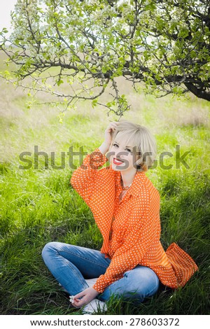 close-up portrait outdoors young beautiful girl in an orange hipster blonde bright cheerful polka dot blouse , smiling red plump lips on the background of green grass