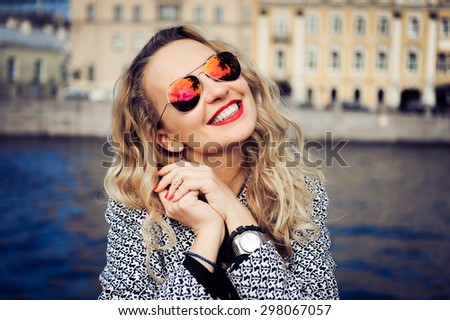 close-up portrait of a young girl hipster beautiful blonde in sunglasses with red lips laughing and posing against the backdrop of the city