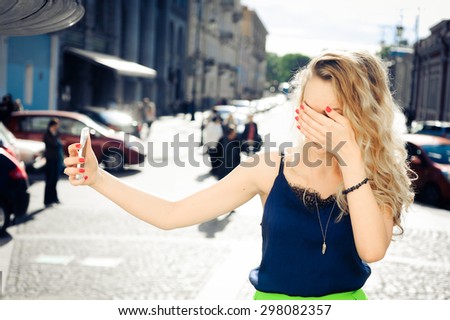 close-up portrait of a beautiful young blonde woman with curly hair with the phone in hand, laughing and posing and makes selfi