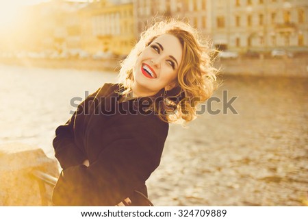 stylish portrait of a beautiful young  curly woman with red lips  on the streets of St. Petersburg in a red blouse on a sunny day at sunset posing and smiling Life Style , \
autumn