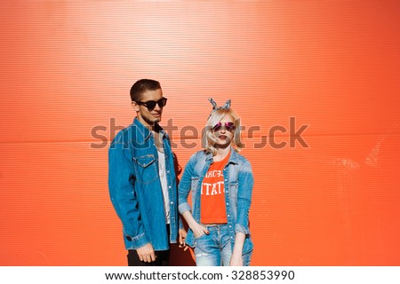 close-up portrait of a beautiful young couple in love bright blonde girl with red lips and a guy with a beard wearing a cap hipsters on a red background smiling and posing lifestyle  in jeans