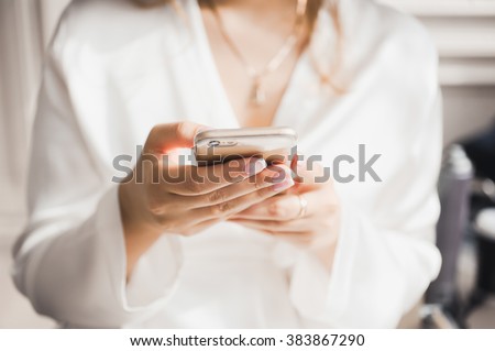Hands close-up in the bright day of a young girl in a silk white coat holding phone smartphone