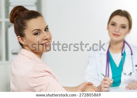 Smiling satisfied young pretty female patient visiting family doctor. Therapeutist reception. Medical concept. Happy patient and attending medical doctor.