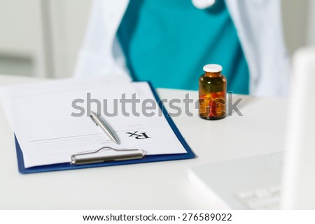 Medical doctor siting in front of working table and writing prescription. Medical and pharmacy concept. Jar of pills on table with prescription.