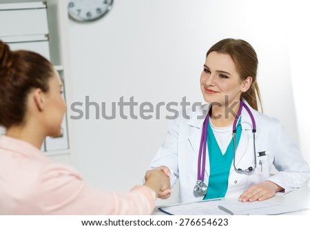Young beautiful smiling female doctor shaking hand with patient. Partnership, trust and medical ethics concept. Handshake with satisfied client.