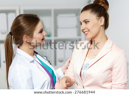 Young beautiful smiling female doctor shaking hand with pretty woman patient. Partnership, trust and medical ethics concept. Handshake with satisfied client.