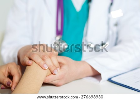 Female doctor\'s hands holding patient\'s hand for encouragement and empathy. Partnership, trust and medical ethics concept. Bad news lessening and support.