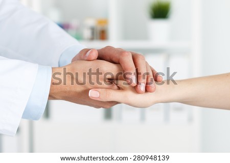 Friendly male doctor\'s hands holding female patient\'s hand for encouragement and empathy. Partnership, trust and medical ethics concept. Bad news lessening and support. Patient cheering and support