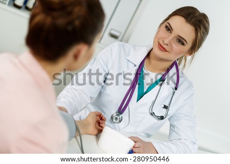 Smiling cheerful female medicine doctor with pretty face measuring blood pressure to patient while chatting her. Patient communicates with physician doctor having medical examination. Medical concept