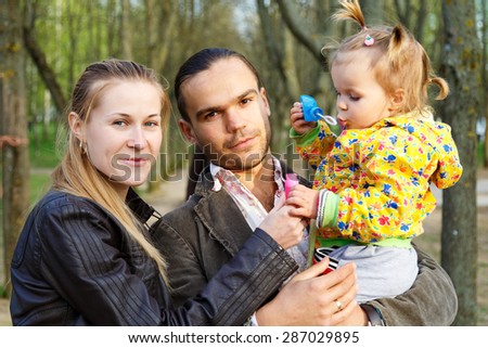 Happy parents with daughter outdoor playing and making soap bubbles. Beautiful smiling woman and handsome man blowing bubbles to cute little girl in city park. Childhood and parenthood concept