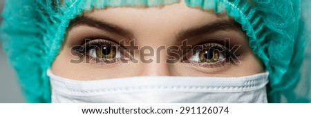 Female doctor's face wearing protective mask and green surgeon's cap closeup. Surgeon's eyes close up gazing intently in camera. Resuscitation and emergency concept. Letterbox view