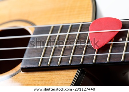Small Hawaiian four stringed ukulele guitar with red pick between strings closeup. Musical instruments shop or learning school concept