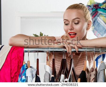 Beautiful blonde woman standing near wardrobe rack full of clothes and choosing dress. Shopping and consumerism or stylist concept. Nothing to wear and hard to decide concept