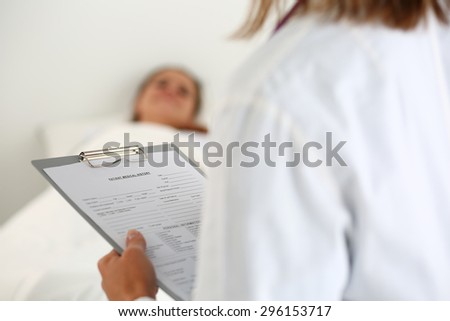 Female medicine doctor filling in patient medical history list during ward round. Medical care or insurance concept. Physician ready to examine patient and help. Patient sleeping