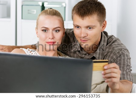 Family couple making shopping over internet looking in notebook and paying with credit card. Husband and wife buying new stuff in house. Shopping, consumerism, delivery and present concept