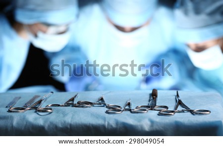 Surgical tools lying on table wile group of surgeons at background operating patient in surgical theatre. Steel medical instruments ready to be used. Surgery and emergency concept