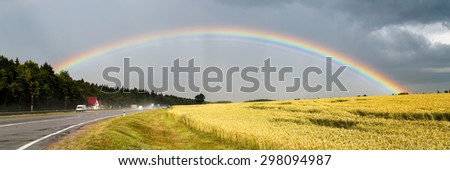 Big beautiful rainbow over highway and cereals field  letterbox view. Rainy day panorama