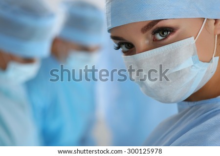 Three surgeons at work operating in surgical theatre. Resuscitation medicine team wearing protective masks saving patient. Surgery and emergency concept. Female surgeon portrait looking in camera