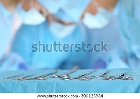 Surgical tools lying on table while group of surgeons at background operating patient in surgical theatre. Steel medical instruments ready to be used. Surgery and emergency concept