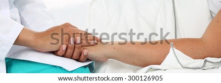 Friendly female doctor hands holding patient hand lying in bed for encouragement, empathy, cheering and support while medical examination. Bad news lessening, compassion. Letterbox view