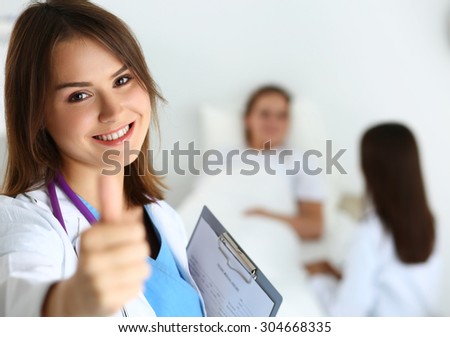 Smiling female medicine doctor holding document pad and showing OK sign with thumb up at ward wile round. Hight level and quality medical service concept. Best treatment and patient care concept
