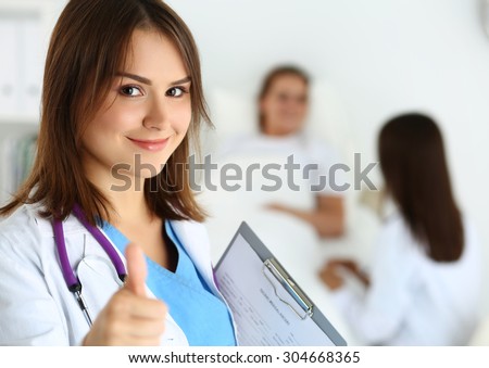 Smiling female medicine doctor holding document pad and showing OK sign with thumb up at ward wile round. Hight level and quality medical service concept. Best treatment and patient care concept