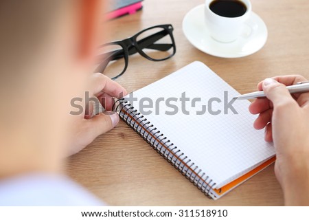 Male hand holding silver pen ready to make note in opened notebook. Businessman or employee at workplace writing business ideas, plans or tasks at personal organizer. Office life or education concept