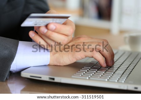 Hands of businessman in suit holding credit card and making online purchase using notebook pc. Shopping, consumerism, delivery or internet banking concept. Anti-fraud and financial security concept
