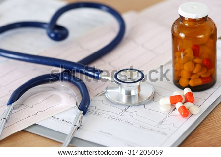 Medical stethoscope head lying on cardiogram chart with pile of pills closeup. Cardiology care, health, protection, prevention and help. Healthy life or insurance concept