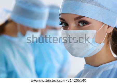 Three surgeons at work operating in surgical theatre. Resuscitation medicine team wearing protective masks saving patient. Surgery and emergency concept. Female surgeon portrait looking in camera