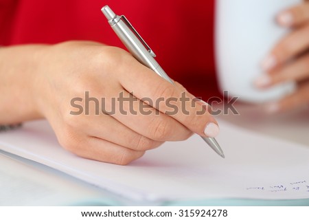 Female hands holding cup of coffee or tea and silver pen closeup. Woman writing letter, list, plan, making notes, doing homework. Student studying. Education, self development and perfection concept