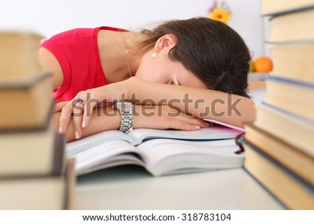 Tired female student at workplace in room taking nap on pile of textbooks. Sleepy brunette woman resting during education after sleepless night. Student in despair caused by exam deadline concept