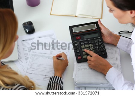 Two female accountants counting on calculator income for tax form completion hands closeup. Internal Revenue Service inspector checking financial document. Planning budget, audit, insurance concept