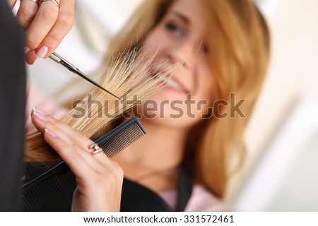 Female hairdresser hold in hand between fingers lock of hair, comb and golden scissors closeup. Hairdresser salon, barber shop, perfect look, new hairdo concept