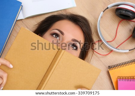 Beautiful woman lying on floor covering face with book dreaming. Female student studying using textbooks. Education, learning, self development, leisure, pastime, library or bookshop concept