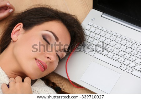 Beautiful woman lying on laptop computer on wooden floor sleeping. Female student taking nap while studying or working. Education, communication, leisure, pastime, preparing for exams concept