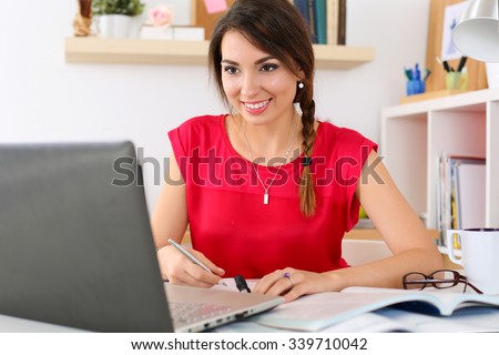 Beautiful smiling female student using online education service. Young woman in library or home room looking in laptop display watching training course. Modern study technology concept