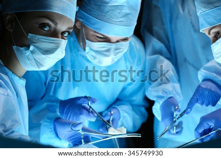 Group of surgeons at work operating in surgical theater. Resuscitation medicine team wearing protective masks saving patient. Surgery and emergency concept. Female surgeon portrait looking in camera